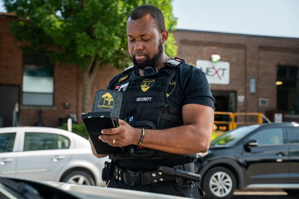 A police officer utilizing mobile security services while using a cell phone in front of a car.