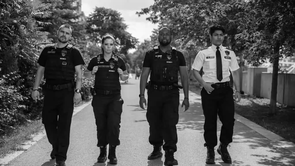 Four police officers, functioning as security guards for hire, are walking down a street.