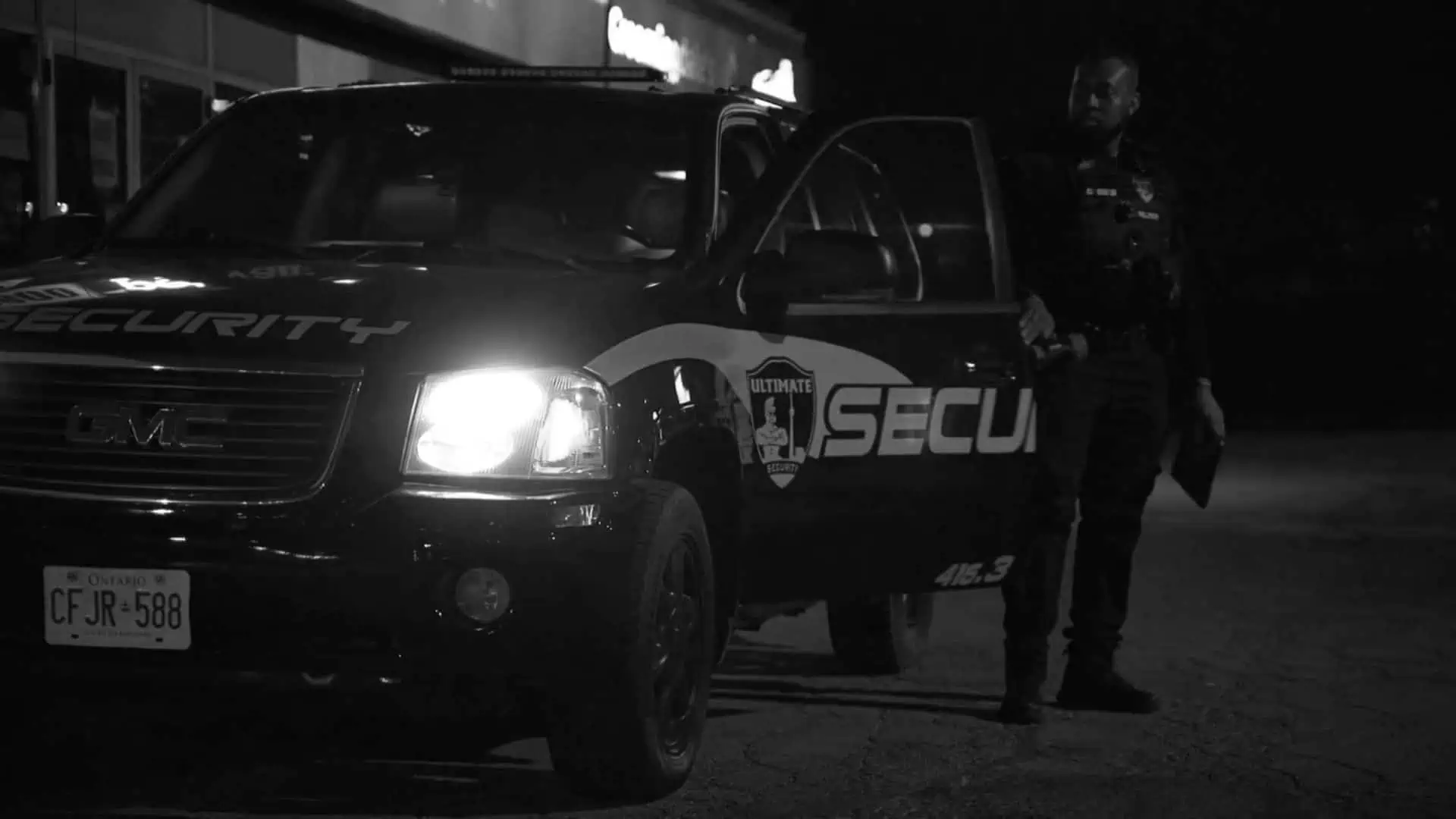 A security officer is conducting mobile patrol security services next to a police car at night.
