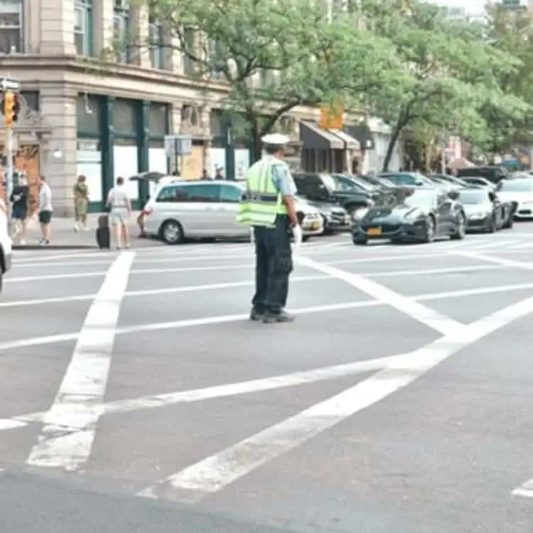A Parking Enforcement Officer in a yellow vest is crossing the street.