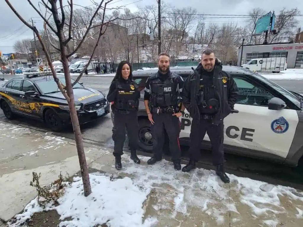 Three police officers providing ultimate security standing next to a police car in the snow.