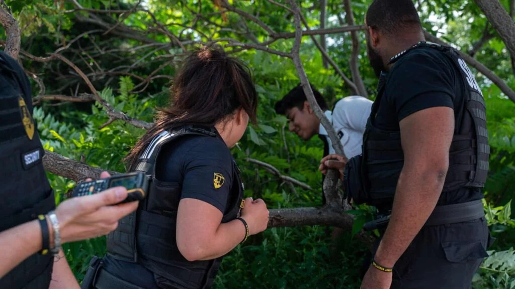 Several uniformed individuals, part of a dedicated Neighborhood Watch team, assist a person near tree branches in a forested area.