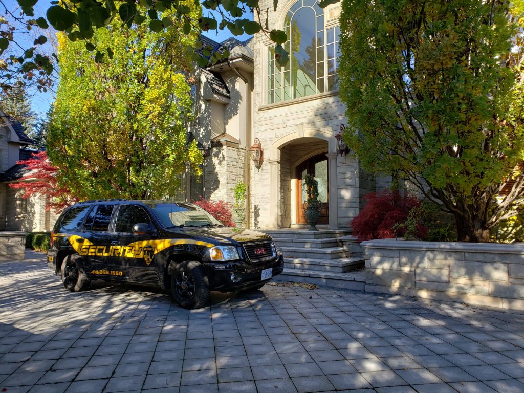 A black Residential Security Services SUV parked in front of an elegant house with autumn-colored trees.