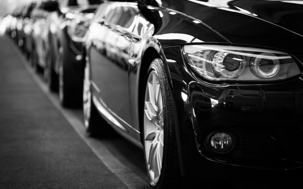 Close-up of the front side of a row of shiny black cars parked in a line, captured in black and white, safeguarding luxury vehicles with timeless elegance.