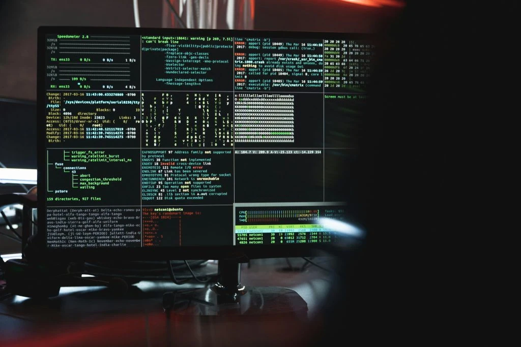 A computer screen displays multiple open terminal windows with various codes, system logs, and performance metrics in a dimly lit room, embodying the rigorous cybersecurity measures essential for high-profile clients.