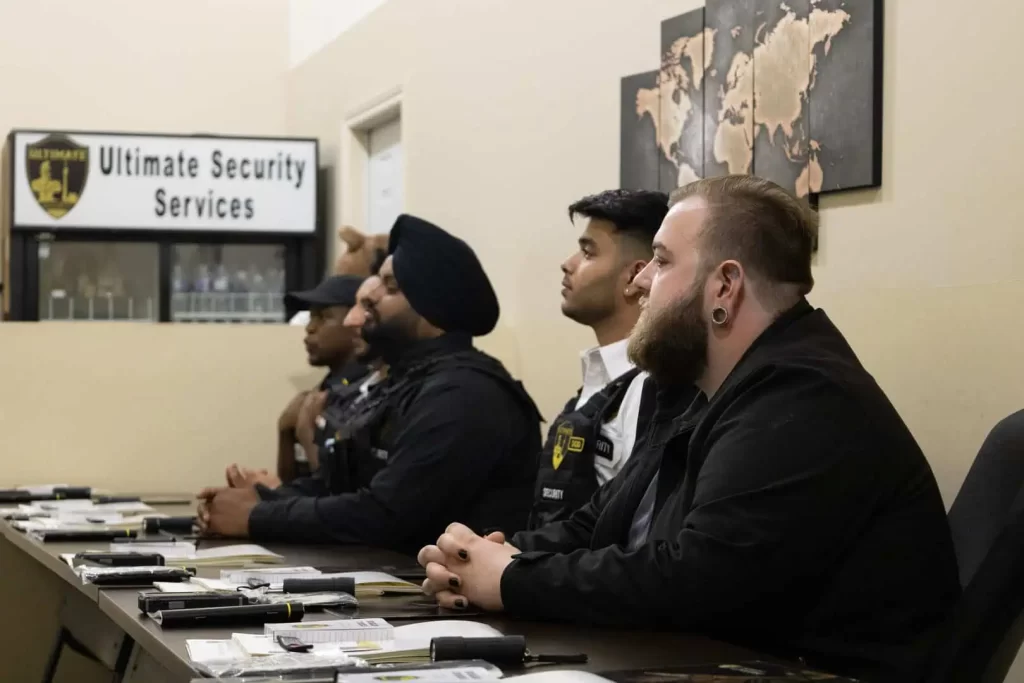 Four security personnel sit attentively at a table during a meeting in a room adorned with maps and a sign reading "Ultimate Security Services," highlighting their expertise as premier security services in Toronto.