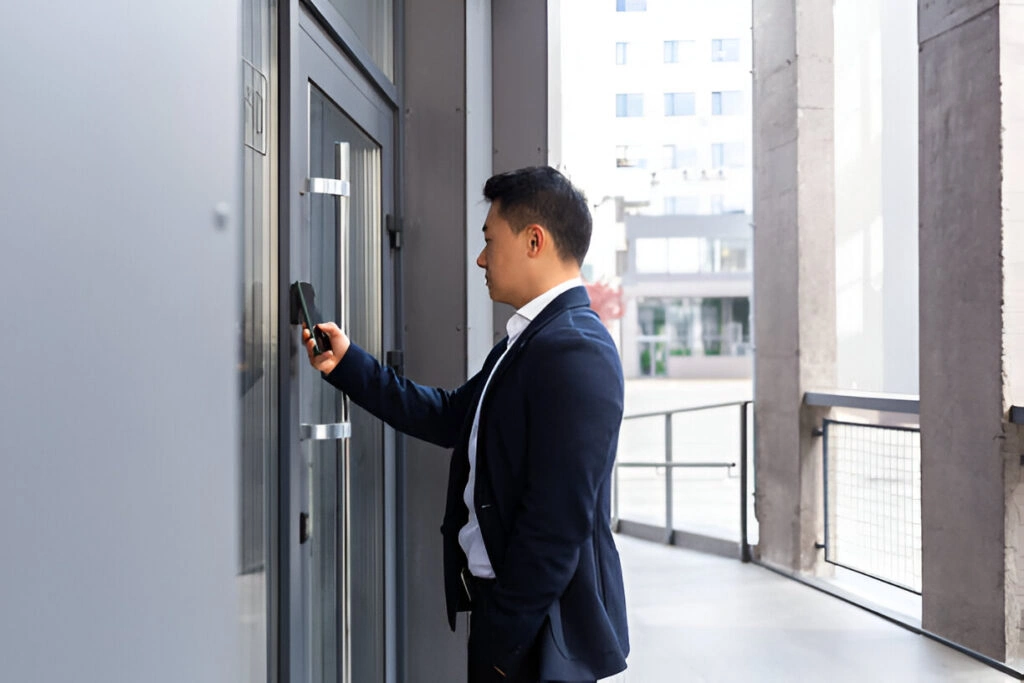 A man in a suit uses a key card to access a glass door in the secure corridor of a modern condominium building.