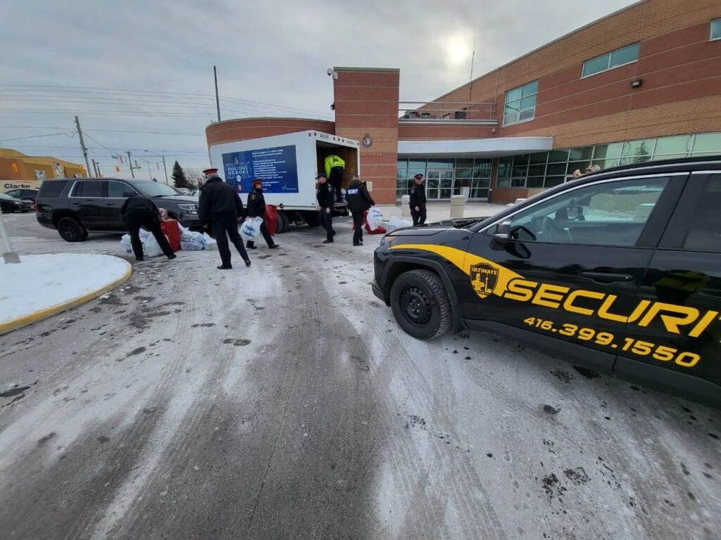 Security personnel and officials, supported by mobile security services, unload items from a truck outside a building on a snowy day. A security vehicle is parked nearby.