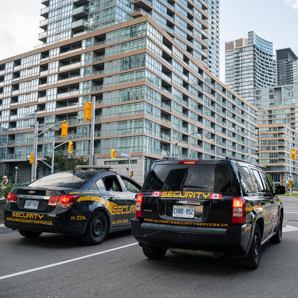 Two black security vehicles are parked at an intersection in front of modern high-rise buildings, highlighting the presence of a Security Guard Near Me in this urban area during daytime.