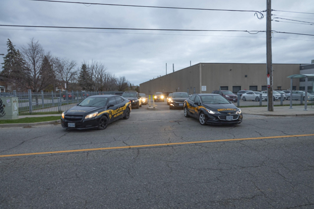 Several security cars are parked and driving near the entrance of a parking lot outside a large industrial building on a cloudy day, showing proactive steps similar to How to Start a Neighborhood Watch in your community.