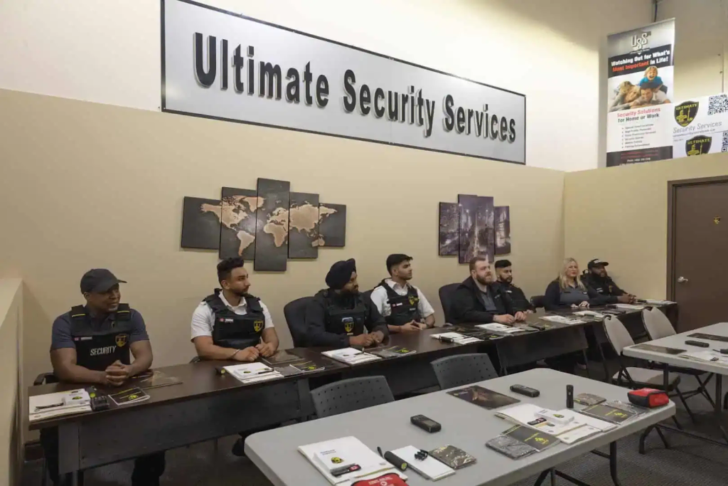 A group of security personnel sits at desks in a classroom under a sign that reads "Ultimate Security Services," participating in basic security guard training in Ontario.