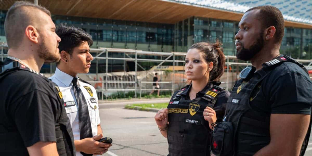 image 2 Four security personnel stand outside a building, engaged in conversation and wearing uniforms and badges, representing professional Security Guard Services.